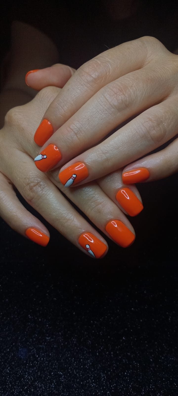 Uñas cuadradas en naranja intenso con pinos de boliche pintados a mano.