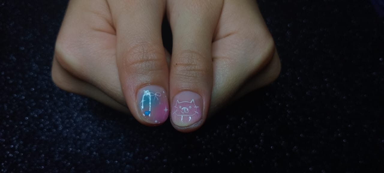 Pulgares con uñas cortas en degradado rosa y azul, con un moño, estrellas y un gatito dibujados en blanco.