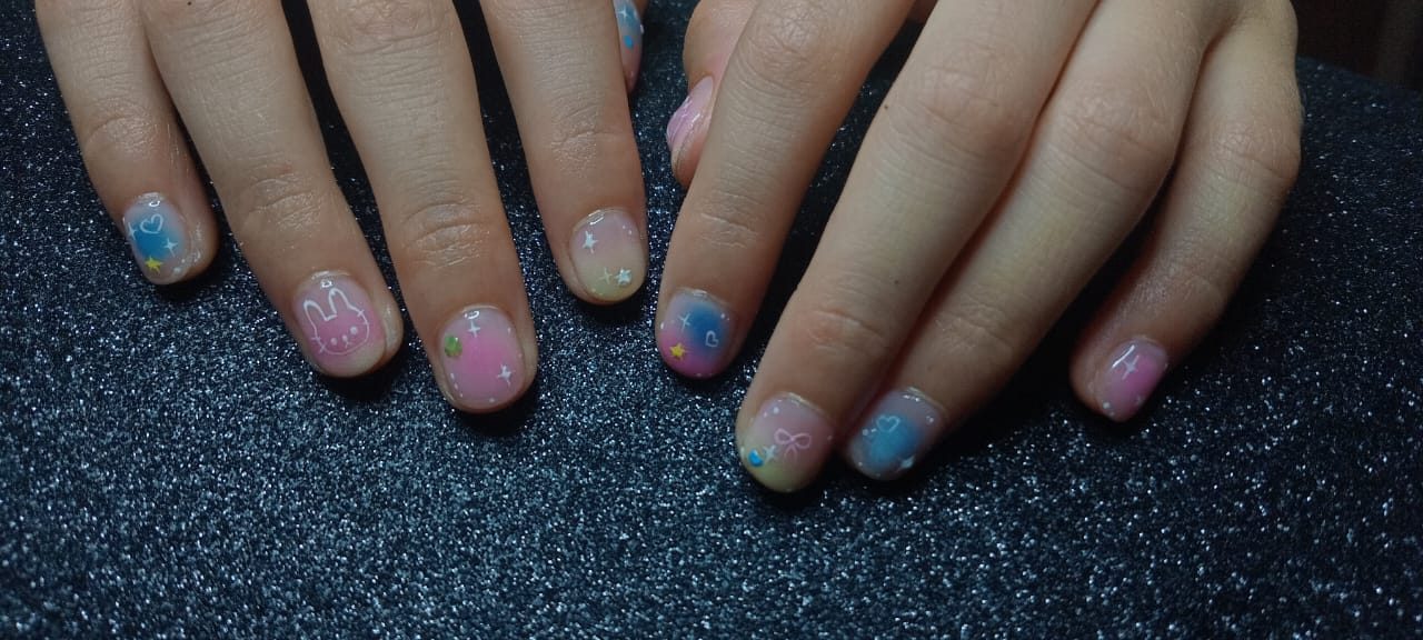 Uñas cortas en degradado pastel rosa, azul y amarillo con un conejito, corazones, moños y estrellas pintados a mano.