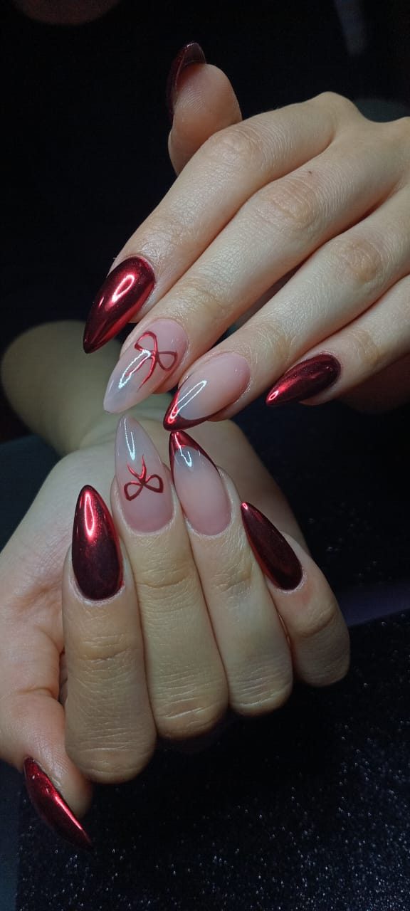 Uñas almendradas largas en cromo rojo espejo, combinadas con nude, francesa roja y moños rojos pintados a mano.