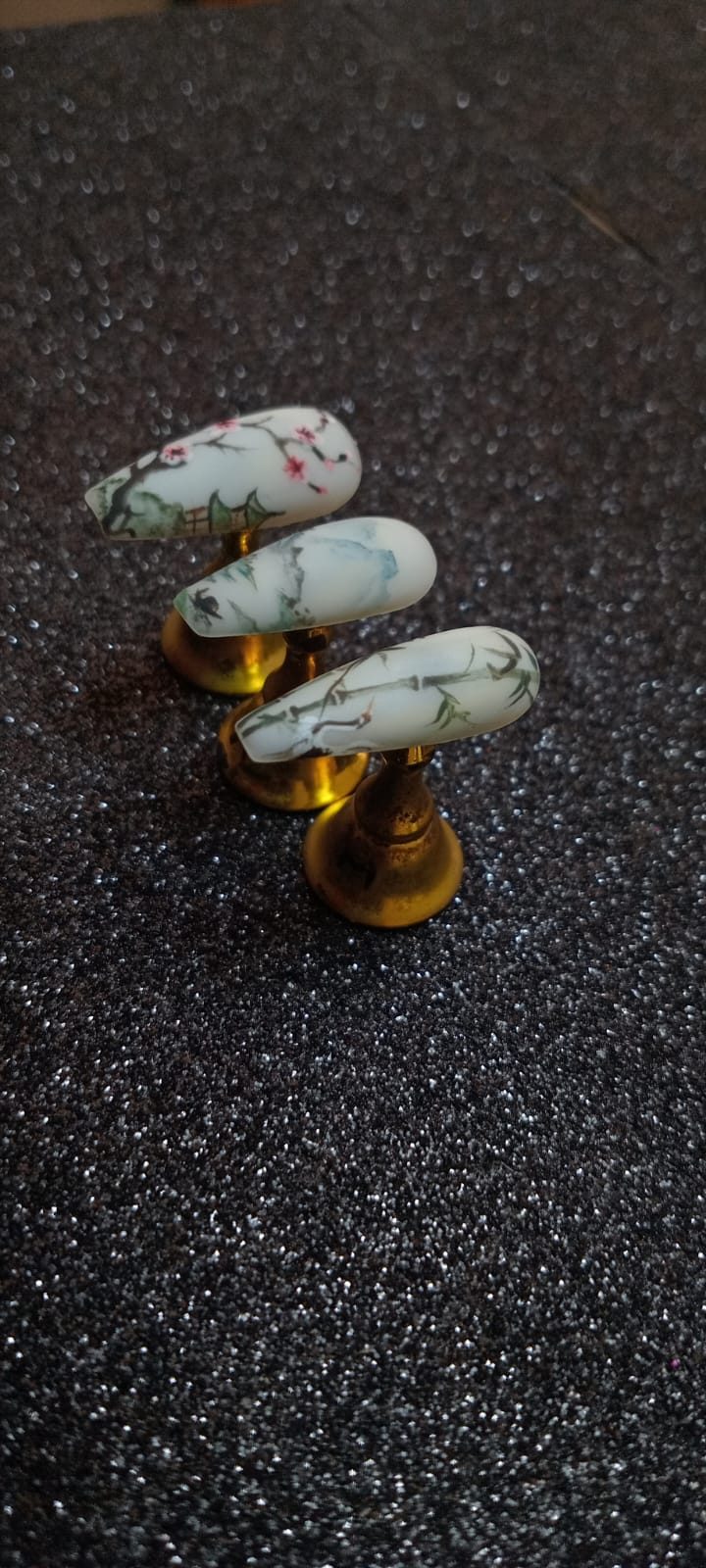 Los mismos tres tips de pintura china, flor de cerezo, montañas y bambú, vistos en diagonal sobre fondo negro brillante.