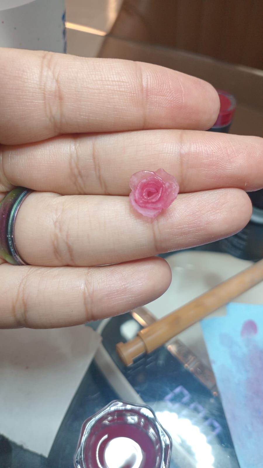 Pequeña rosa esculpida en gel 3D, en tonos rosa, sostenida sobre los dedos para mostrar su tamaño.