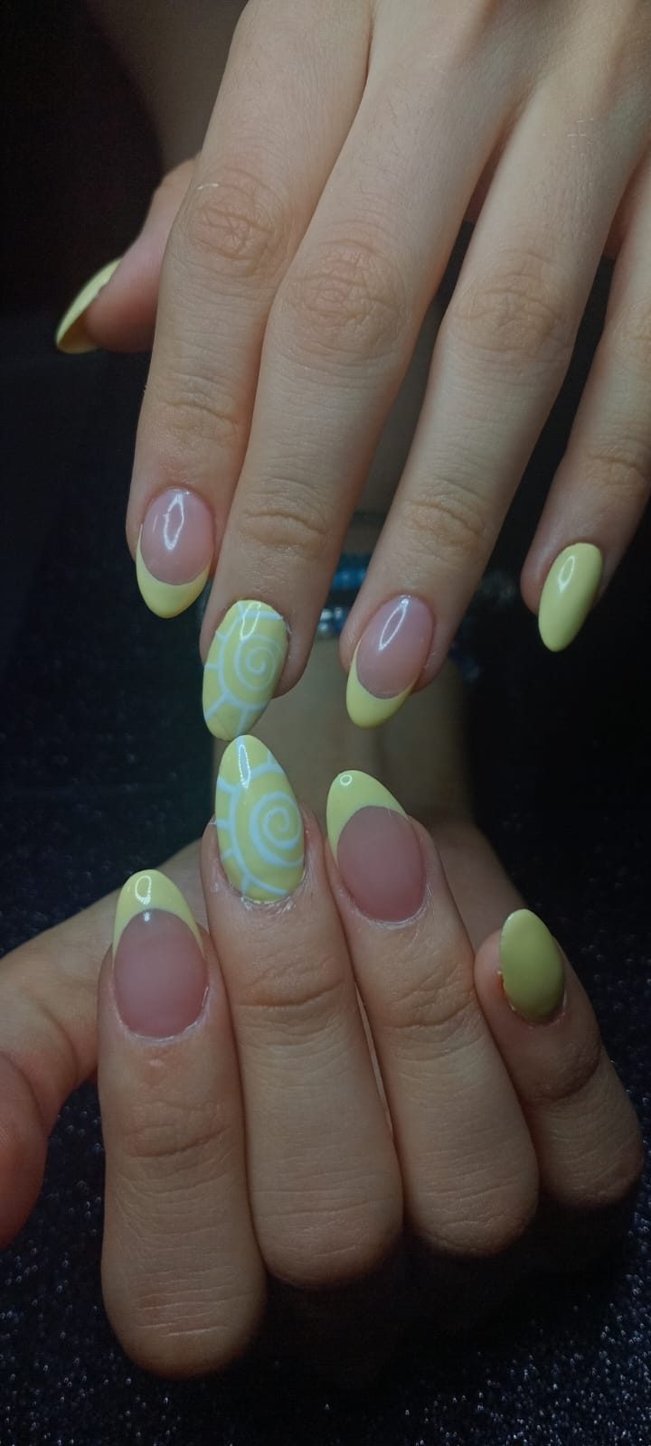 Uñas almendradas con francesa amarillo pastel, una uña amarilla completa y dos con soles en espiral blanca.